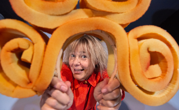 Person i röd klänning håller upp orange, spiralformade föremål nära kameran och ler.