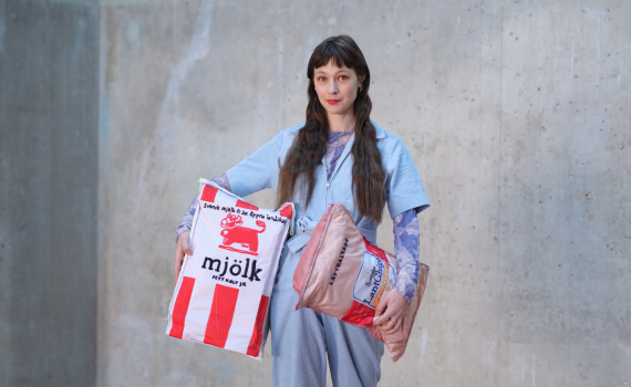 Person i ljus overall bär tygkassar formade som livsmedelsförpackningar, några ligger på golvet runtom.