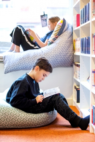 Två barn sitter och läser böcker på bibliotek TioTretton. 