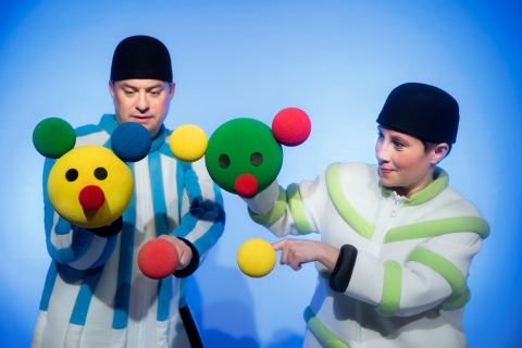 Två dockskådespelare håller i bollar i olika färger, de bilder formen av ansikten och huvuden. 