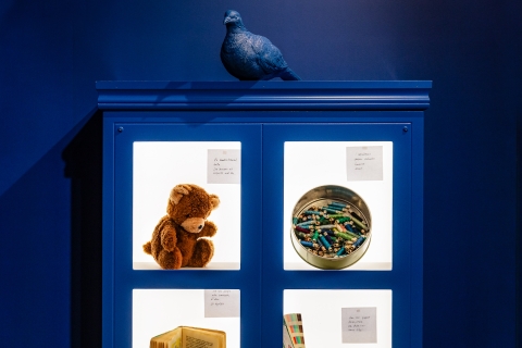 Ett blått skåp med bilder på en nalle, färgkritor, en bok med mera. 