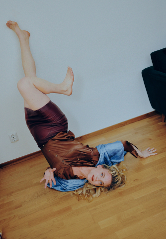 Kvinna i 30–40-årsåldern ligger på golvet med benen upp mot väggen, iklädd brun klänning med blå detaljer.