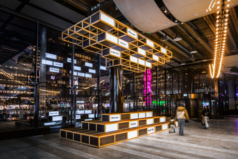 Ljusinstallation sedd från sidan med texter som "Minnet" och "med flit", kvinna med barn i förgrunden.