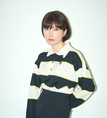 Mieko Kawakami står mot en ljus bakgrund i ett minimalistiskt porträtt med tydliga kontraster och ett lugnt, fokuserat uttryck.