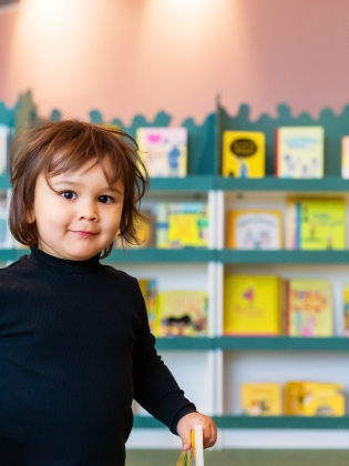 Ett barn framför bokhyllor i bibliotek Rum för Barn.  