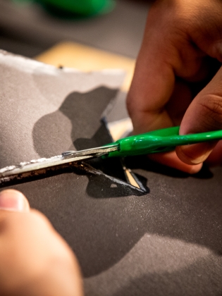 En person klipper med sax i papper, för att skapa en stavdocka. 