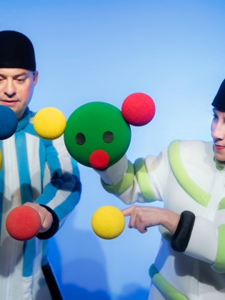 Två dockskådespelare håller i bollar i olika färger, de bilder formen av ansikten och huvuden. 