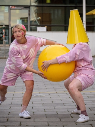 Två personer som håller i en gul boll, den ena har en gul tratt på huvudet.