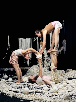Tre cirkusartister som utför akrobatik bland massa garn