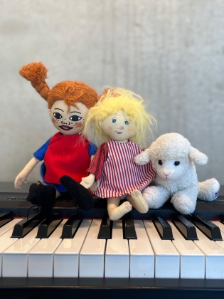 Två dockor och en nalle sitter på ett piano. 