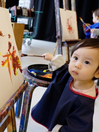 Ett barn står vid ett staffli och målar en tavla. 