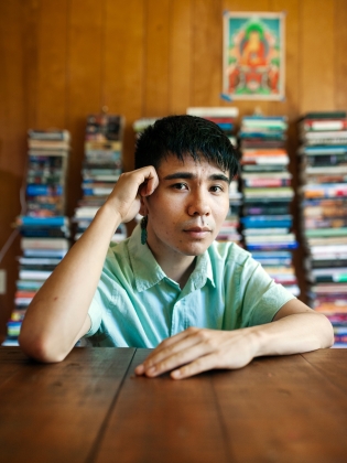 Författaren Ocean Vuong sitter vid ett bord, i bakgrunden syns staplar med böcker.