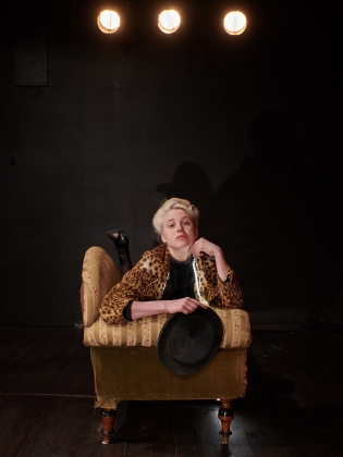 En kvinna i leopardpäls och en hatt i handen som ligger i en soffa