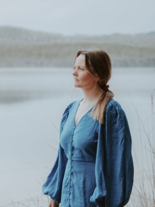 En kvinna i blå klänning framför en sjö