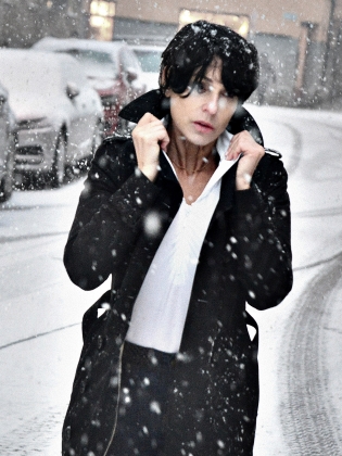 En kvinna står utomhus i snön och fäller upp kragen på sin rock. 