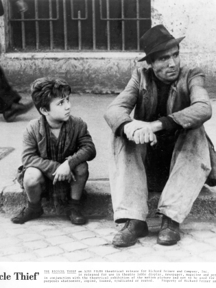 Svartvitt foto på en man och en pojke som sitter bredvid varandra på en trottoar. 
