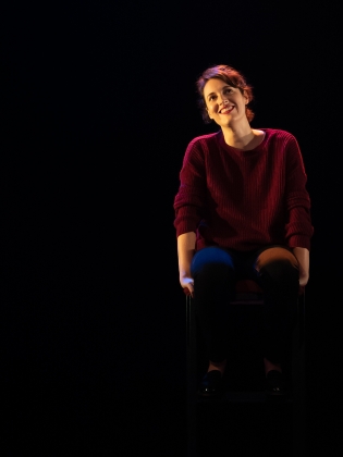 En kvinna i röd tröja sitter på en scen