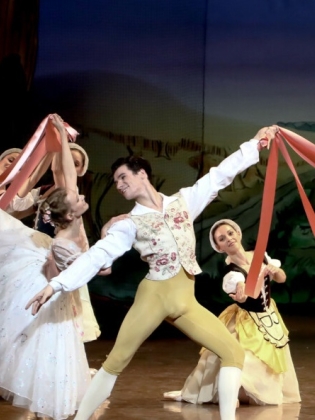 En balettensemble i klassiska kostymer dansar på en scen