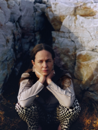 En kvinna på huk framför en stenvägg