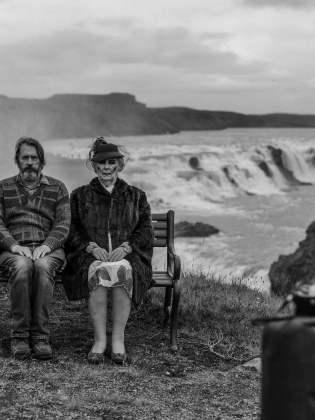 Ett par sitter på en bänk med ett isländskt landskap i bakgrunden