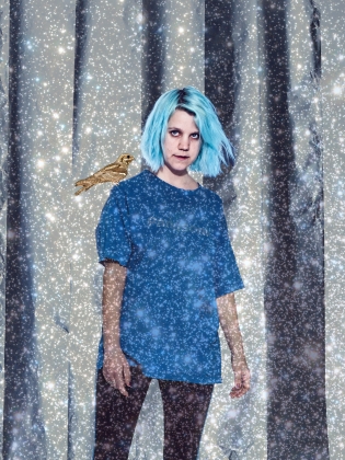 En person med blått långt hår, med en guldfärgad fågel på axeln, omgiven av ett stjärnliknande skimmer. 