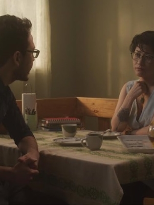 En man och en kvinna sitter vid ett köksbord med kaffekoppar på