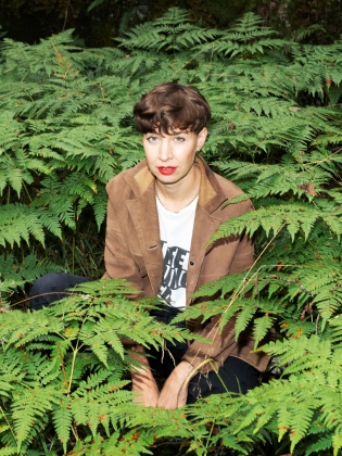 En kvinna sitter i ett buskage av ormbunkar