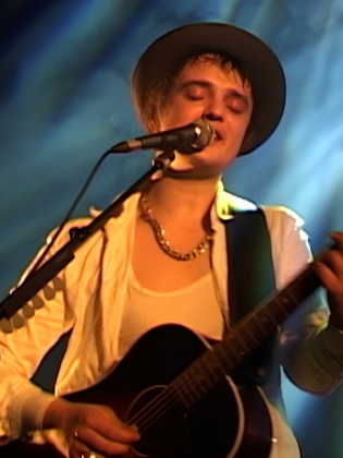 En man i hatt spelar gitarr och sjunger på en scen