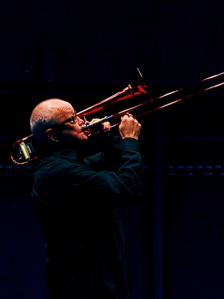 En man mot mörk bakgrund spelar en röd trombon