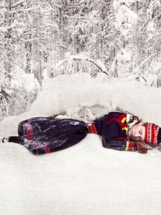 En person klädd i samedräkt ligger ner i snön. 