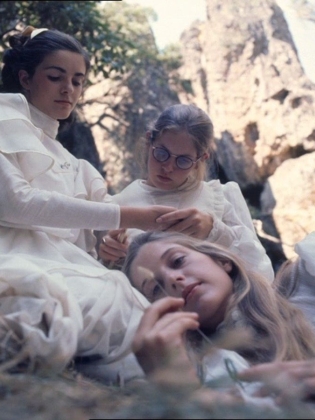 Tre flickor i 1800-talskläder ligger på en äng