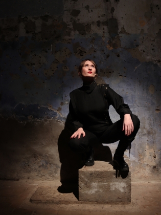 En kvinna klädd i svart sitter i ett rum i sten och betong. 