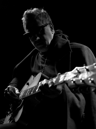 Svartvit bild på man i hatt med gitarr