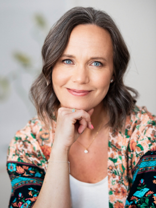 Kvinna i 40–50-årsåldern med axellångt brunt hår och blommig kimono poserar med handen mot hakan.