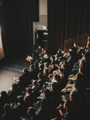 En fullsatt salong med publik som tittar mot en upplyst scen.