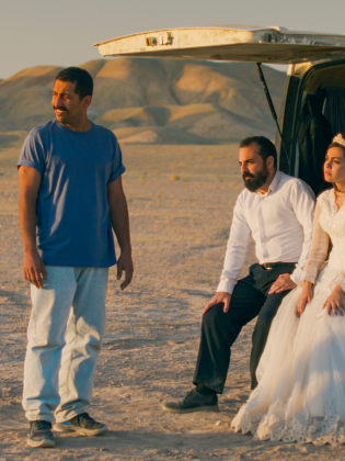 Tre personer sitter i bagageluckan på en vit van i öknen.