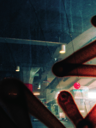 Abstrakt bild genom glas med suddiga ljus, taklampor och mörka former i förgrunden som delvis skymmer en inomhusmiljö.