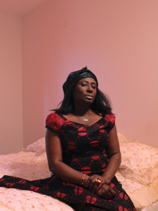 En kvinna sitter på en säng i ett rosa rum.