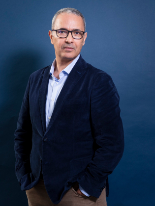 Man i 50–60-årsåldern med kort grått hår och glasögon, i blå kavaj mot blå bakgrund.