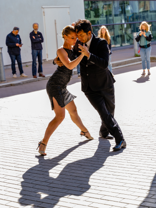 Två personer som dansar tango på ett torg och lite publik som ser på.
