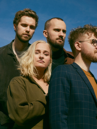 De fyra musikerna framför en blå himmel
