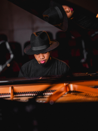 En person med hatt och svarta kläder spelar piano