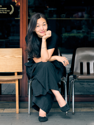 Lee Chia-Ying sitter utanför ett café i ett avslappnat och varmt porträtt där miljön ger bilden en vardaglig och inbjudande ton.