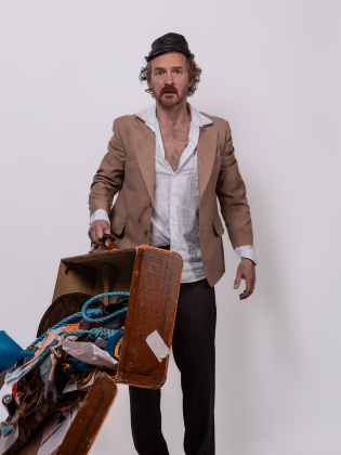 Man med keps och mustasch står bredvid en öppen resväska fylld med olika föremål.