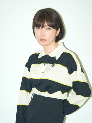 Mieko Kawakami står mot en ljus bakgrund i ett minimalistiskt porträtt med tydliga kontraster och ett lugnt, fokuserat uttryck.