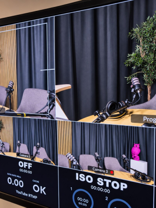 Bildskärm visar flera kameravyer av podcaststudion med mikrofoner, två fåtöljer och en rosa ugglefigur.